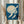 May include: Person in cream ruffled sleeves holding framed vintage Japanese art print featuring white cranes flying across deep blue sky with large pale moon. Print shows traditional woodblock style with textural brushwork at bottom. Person also holds dried pampas grass stems. Soft neutral curtains and lighting in background create serene styling scene.