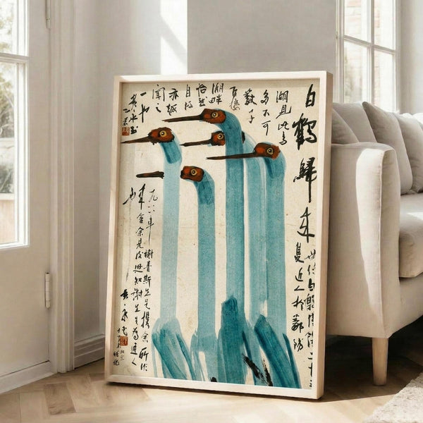 May include: Framed traditional Chinese watercolor painting showing five long-necked cranes with turquoise blue bodies, reddish-brown heads, and black beaks, surrounded by Chinese calligraphy text on cream paper. The artwork leans against a white wall beside a beige sectional sofa in a bright room with large windows and hardwood floors.