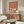 May include: Japanese-inspired artwork featuring three elegant white cranes with black wing tips and long necks, set against a warm terracotta orange background with horizontal bands at the bottom. The framed poster hangs above a mid-century modern walnut credenza in a minimalist living room with cream walls, white upholstered chair, glass-top coffee table, and contemporary lighting fixtures.