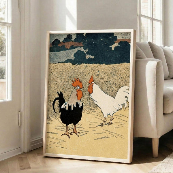 May include: Vintage-style artwork print showing two roosters - one black with red comb and one white - standing on sandy ground beneath a dramatic cloudy sky. The illustration has a textured, grainy appearance reminiscent of mid-century printmaking. Displayed in a light wood frame leaning against a white wall next to a beige upholstered chair in a bright, minimalist living room with large windows.