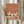 May include: Person holding framed poster print featuring three elegant white cranes with black wing tips and long legs standing on terracotta orange background with horizontal striped border. Light wood frame, hands in beige ruffled sleeves, dried pampas grass visible, neutral curtained interior setting.