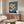 May include: Japanese woodblock print artwork displayed above a wooden sideboard in a modern living room. The artwork features white cranes flying across a blue sky with a golden moon, framed in natural wood. Room includes cream walls, white curved chair, oval glass coffee table, and minimalist decor with warm wood tones throughout.