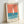 Framed vintage-style poster featuring a minimalist sailboat design with coral orange sky and teal blue water. The white sailboat has geometric triangular sails and sits above stylized horizontal wave lines. Text at bottom reads "MADE IN USSR IMPREGNATED SAFETY MATCHES" in dark letters. The print has a cream-colored background with speckled texture and is displayed in a light wood frame, leaning against a white wall.
