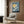 May include: A framed vintage Japanese woodblock print featuring white cranes flying against a blue sky with golden moon, displayed on wood-paneled wall above a cream upholstered armchair with geometric pillow. Modern floor lamp and round side table with open book complete the elegant reading nook scene.