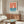 May include: Vintage-style poster with coral pink sky, blue water, and white sailboat hung above a walnut credenza in modern living room. Black thin frame, white matting. Room features cream walls, white curved chair, oval glass coffee table, brass floor lamp, and natural lighting from window.