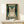 May include: Framed poster featuring a tabby cat wearing black headphones on teal background with cream text and musical note decorations, displayed on light wood shelf next to small white gift box against white wall
