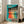 May include: Framed vintage-style poster with turquoise background showing six women in colorful dresses dancing in a line, with "Dance more" text at top. White wooden frame leans against wall next to beige upholstered chair in bright room with white walls and windows.