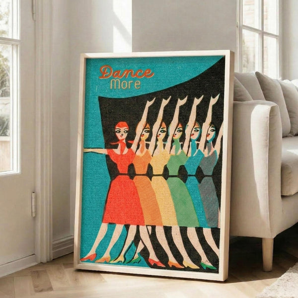 May include: Framed vintage-style poster with turquoise background showing six women in colorful dresses dancing in a line, with "Dance more" text at top. White wooden frame leans against wall next to beige upholstered chair in bright room with white walls and windows.