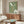 May include: Green vintage-style poster with white squid illustration and Japanese text displayed above wooden sideboard in modern living room. Cream upholstered chair and glass coffee table with blue accent visible. Poster shows retro seafood design with abalone shell graphic in earthy sage green color with white and orange text elements.