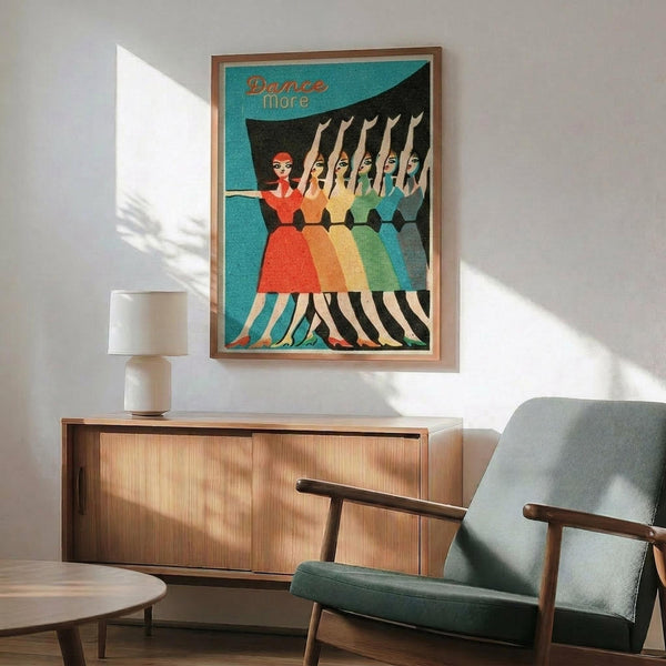 May include: Mid-century modern living room with teal and wood furniture featuring a framed vintage-style poster showing five dancing women in colorful dresses - red, orange, yellow, green, and blue - with "Dance More" text on turquoise background, displayed above wooden sideboard next to white ceramic lamp and sage green upholstered chair with wooden arms.