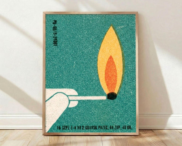 May include: Framed vintage Polish poster print leaning against white wall on light wood floor. Teal textured background with minimalist illustration of white hand holding lit match with yellow and orange flame. Black Polish text at top and bottom. Simple wooden frame in natural finish.