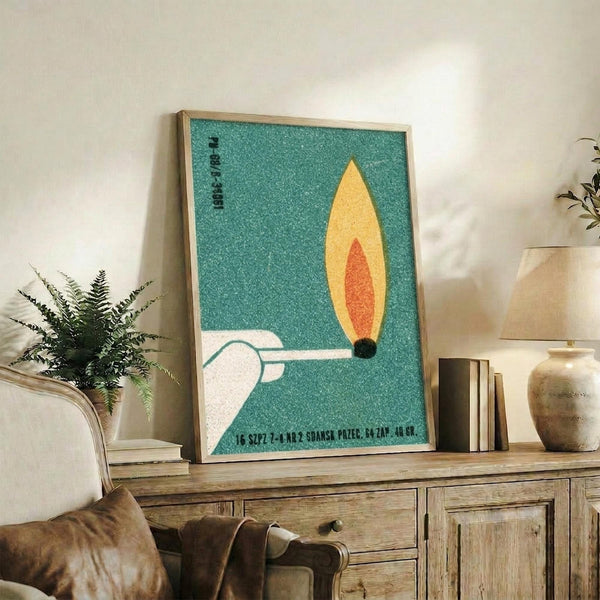 May include: Mid-century modern poster with turquoise textured background featuring a yellow and orange flame design above white geometric shapes, displayed in light wood frame on rustic wooden sideboard alongside fern plant, books, ceramic vase, and beige armchair in cozy living room setting with neutral walls