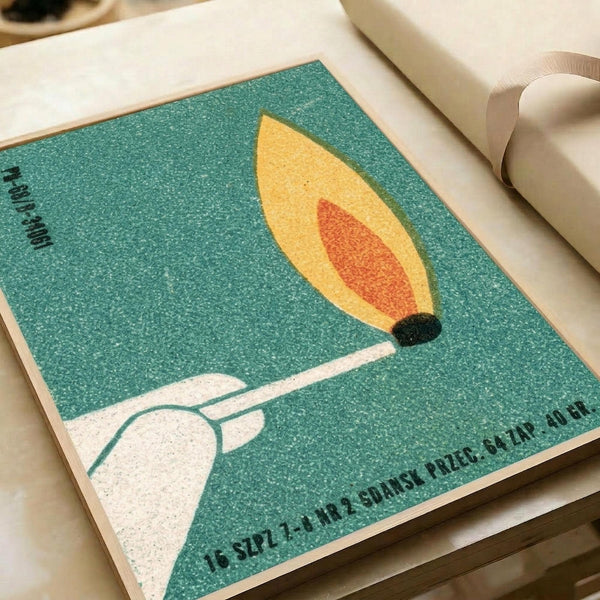 May include: Vintage Polish matchbox label artwork displayed on white paper with cream ribbon nearby. Features a stylized leaf design in yellow and orange on teal speckled background, with white hand silhouette below. Text appears in Polish along edges. Retro mid-century modern aesthetic with grainy textured printing style typical of 1960s Eastern European design.