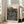 May include: A framed art poster featuring bold black polka dots and flowing striped patterns on cream background, displayed in bright living room corner beside beige sofa. Poster shows orange and black text reading "YAYOI KUSAMA" at top with Japanese characters, and "MUSEE D'ART MODERNE DE LA VILLE DE PARIS" at bottom. Natural wood frame leans against white wall with tall windows casting soft shadows.
