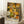 May include: Framed art print with colorful floral pattern in yellow, orange, green, white and brown tones featuring circular dotted flowers and polka dots, displayed leaning against white wall on white textured rug next to wooden side table with coffee cup and beige throw blanket