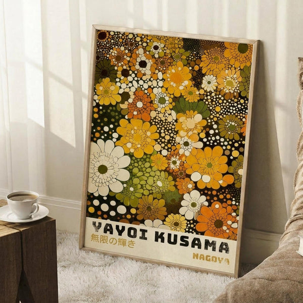 May include: Framed art print with colorful floral pattern in yellow, orange, green, white and brown tones featuring circular dotted flowers and polka dots, displayed leaning against white wall on white textured rug next to wooden side table with coffee cup and beige throw blanket