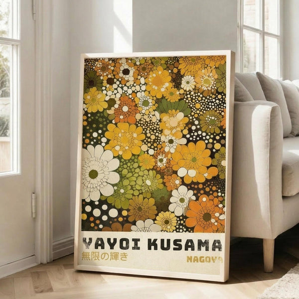 May include: Framed poster with colorful floral pattern in yellow, orange, green, and white tones featuring dotted circles and daisy-like flowers against dark background, displayed on wooden floor next to beige upholstered chair in bright living room with white walls and large windows
