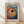 May include: Framed poster print featuring a vibrant fish artwork in Kusama's distinctive polka dot style. The fish has a large circular eye and is covered in colorful dots against a swirling background of blues, oranges, and reds. Text reads "YAYOI KUSAMA" at top with Japanese characters below. Natural wood frame sits on light wooden floor against white wall with soft shadows.