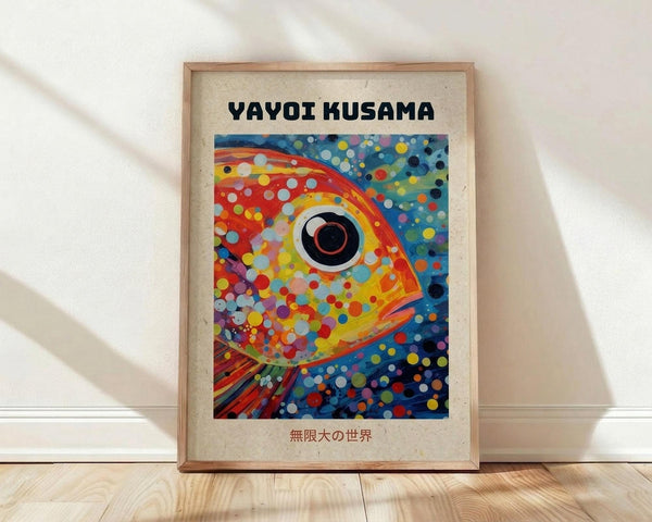May include: Framed poster print featuring a vibrant fish artwork in Kusama's distinctive polka dot style. The fish has a large circular eye and is covered in colorful dots against a swirling background of blues, oranges, and reds. Text reads "YAYOI KUSAMA" at top with Japanese characters below. Natural wood frame sits on light wooden floor against white wall with soft shadows.