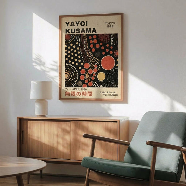 May include: Framed Yayoi Kusama exhibition poster with black background featuring red, orange and cream polka dots in organic flowing patterns, displayed above a wooden sideboard with white ceramic lamp in a mid-century modern living room with mint green upholstered armchair and round wooden coffee table, natural sunlight casting shadows on white wall