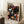 May include: Framed art poster featuring colorful polka-dotted mushrooms and organic shapes on black background, displayed leaning against white wall next to wooden side table with coffee cup. The vintage-style exhibition poster shows vibrant pink, orange, blue and white circular patterns with Japanese text. Light wood frame surrounds the artwork in a cozy interior setting with textured rug and beige throw blanket visible.