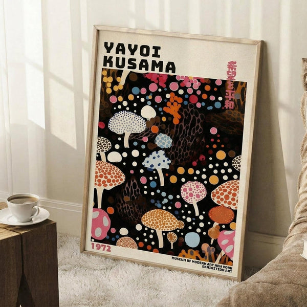 May include: Framed art poster featuring colorful polka-dotted mushrooms and organic shapes on black background, displayed leaning against white wall next to wooden side table with coffee cup. The vintage-style exhibition poster shows vibrant pink, orange, blue and white circular patterns with Japanese text. Light wood frame surrounds the artwork in a cozy interior setting with textured rug and beige throw blanket visible.