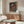 May include: Colorful mushroom poster with psychedelic design featuring vibrant red, orange, and blue fungi against dark starry background, displayed in light wood frame above mid-century modern walnut credenza. White sculptural chair and glass oval coffee table complete the minimalist living room scene with cream walls and natural lighting.