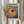 May include: Person holding framed art print featuring colorful abstract fish with large eye, vibrant dots and circles in rainbow colors against blue background, displayed in light wooden frame. Dried pampas grass visible beside figure wearing cream colored clothing with ruffled sleeves in bright interior setting.