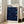 May include: Framed art print with deep blue swirling background filled with white dots and colorful circular planets in yellow, turquoise, and blue tones. Bold black text reads "YAYOI KUSAMA" at top with red Japanese characters and "1991" at bottom. Light wood frame leans against white wall next to beige upholstered chair in bright, minimalist living room with large windows.
