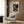 May include: A vintage-style art poster featuring colorful polka-dotted mushrooms on black background, displayed in light wooden frame on wood-paneled wall. Modern beige armchair with geometric patterned pillow sits below, alongside brass floor lamp and dark side table with open book. Neutral tones throughout the contemporary interior setting.