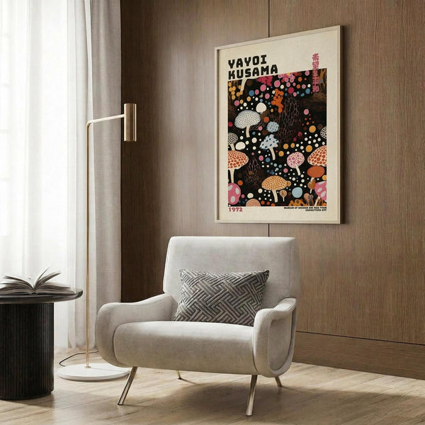 May include: A vintage-style art poster featuring colorful polka-dotted mushrooms on black background, displayed in light wooden frame on wood-paneled wall. Modern beige armchair with geometric patterned pillow sits below, alongside brass floor lamp and dark side table with open book. Neutral tones throughout the contemporary interior setting.
