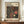 May include: Framed exhibition poster featuring Yayoi Kusama's signature polka dot artwork in black background with coral red, cream and yellow circular patterns and flowing dotted lines. Text shows Tokyo 1998 and April 1986 dates with Japanese characters. Displayed on wooden console table beside white ceramic vase and books against cream walls with white trim molding.