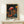 May include: Framed poster with vibrant psychedelic mushroom illustration featuring colorful spotted fungi in pink, orange, and blue against starry black background. Artwork shows detailed stems and caps with polka dot patterns reminiscent of Japanese pop art style. Natural wood frame sits on light wooden surface next to small white wrapped gift box. Clean white wall background creates minimalist display setting.