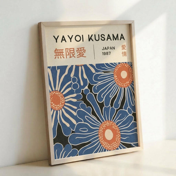 Framed art print featuring stylized blue flowers with orange centers and white dotted details on cream background. Japanese characters and "JAPAN 1987" text at top. Light wood frame leaning against white wall, casting soft shadow.