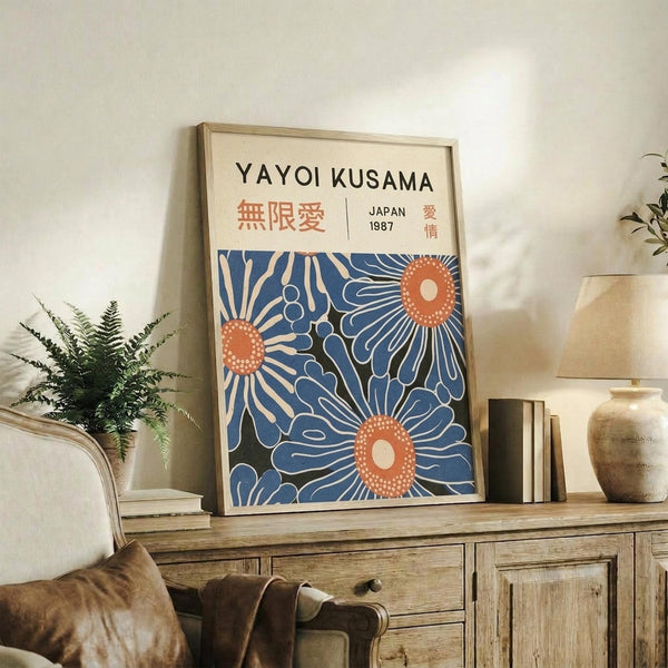 May include: Framed art print with cream background featuring blue floral design and orange circular elements, displayed on rustic wooden sideboard alongside decorative pottery, books, and fern plant in neutral-toned living room setting with beige upholstered furniture