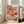 May include: Framed art print leaning against white wall next to beige upholstered chair in bright living room. Poster features colorful abstract pattern of overlapping circular shapes in coral, pink, orange, mint green, and black with polka dots and geometric textures. Black text at top with Japanese characters, date 1981 at bottom. Light wood frame, cream matting. Natural lighting from windows creates soft shadows on white walls and light wooden floors.