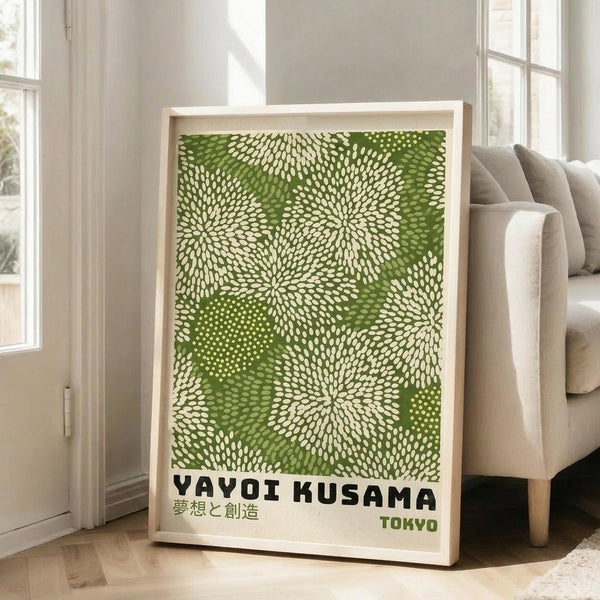 May include: Framed poster with green and white dotted pattern resembling organic burst shapes, displayed in light wood frame leaning against white wall next to beige upholstered sofa. Japanese text visible below main design with "TOKYO" in green letters. Bright natural lighting from nearby windows creates soft shadows on hardwood flooring.