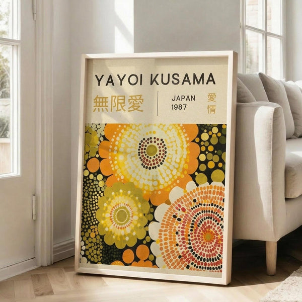 May include: Framed art print leaning against white wall next to beige sofa in bright living room. Poster features colorful dotted circular patterns in yellow, orange, and white on dark background with Japanese text and "JAPAN 1987" at top. Light wood frame, hardwood floors visible.
