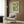 May include: Green botanical poster with white dotted circular patterns and Japanese text, displayed in white frame on wood-paneled wall. Modern beige armchair with geometric patterned pillow, brass floor lamp with white marble base, and dark round side table with open book. Neutral contemporary interior with natural lighting.