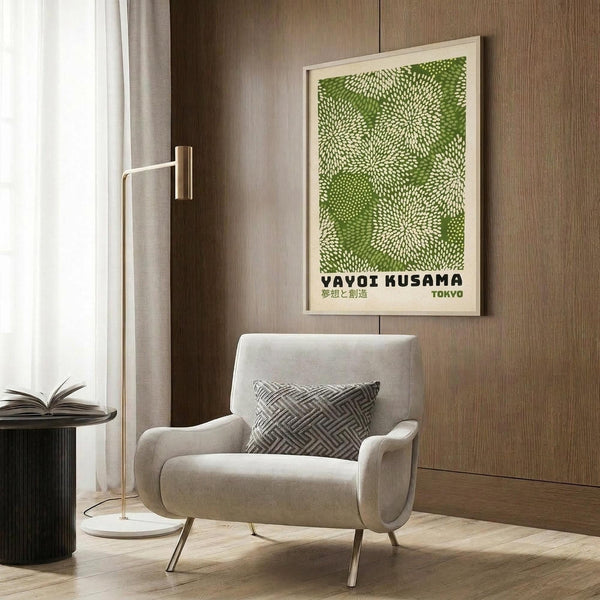 May include: Green botanical poster with white dotted circular patterns and Japanese text, displayed in white frame on wood-paneled wall. Modern beige armchair with geometric patterned pillow, brass floor lamp with white marble base, and dark round side table with open book. Neutral contemporary interior with natural lighting.