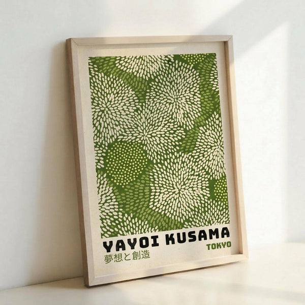 May include: Framed poster with green and cream dotted pattern resembling organic burst or floral motifs, displayed in light wood frame against white wall. Text reads "YAYOI KUSAMA" with Japanese characters below and "TOKYO" in smaller green text. The artwork features radiating circular dot patterns in various shades of green on cream background, creating a nature-inspired abstract design.