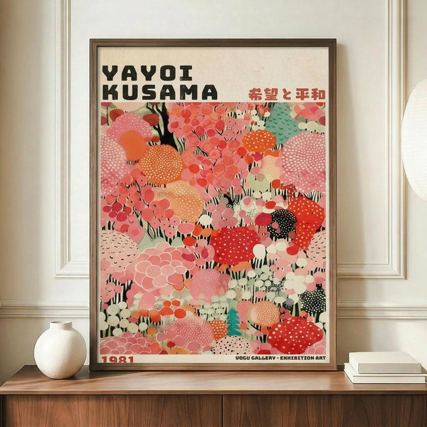 May include: Framed poster with colorful abstract polka dot pattern in coral, pink, orange, and teal tones displayed on wooden sideboard. White ceramic vase and stacked books sit nearby. The artwork features organic spotted shapes with Japanese text at top and "1981" at bottom. Warm neutral wall and elegant molding visible in background.