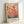Framed art print featuring colorful abstract botanical design with circular balloon-like forms on stems in warm reds, oranges, and yellows transitioning to cool blues and greens at bottom. Japanese text and "YAYOI KUSAMA" printed below artwork. Light wood frame against white wall, leaning on white surface with soft natural lighting.