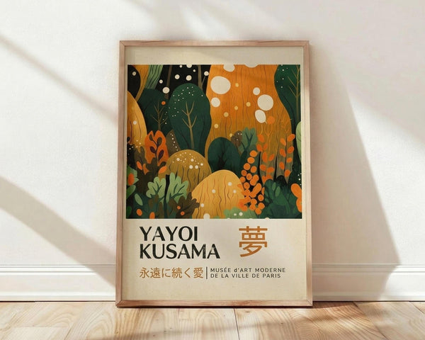May include: Framed poster print leaning against white wall on light wood floor. Features abstract botanical illustration with green leaves, orange and yellow mushrooms, white dots scattered throughout on dark background. Text reads "YAYOI KUSAMA" with Japanese characters and "MUSÉE d'ART MODERNE DE LA VILLE DE PARIS" below colorful nature scene. Natural wood frame with cream matting, soft window light creating shadows on textured white wall.