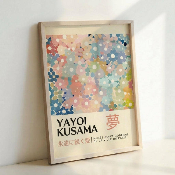May include: Framed museum-style poster with abstract polka dot pattern in soft pastels - coral, blue, mint, and cream circles overlapping across white background. Features "YAYOI KUSAMA" text with Japanese characters and "MUSÉE D'ART MODERNE DE LA VILLE DE PARIS" below. Natural wood frame leaning against white wall, creating gentle shadows.
