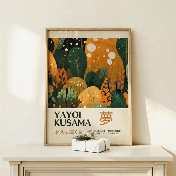 May include: Framed poster with vibrant abstract forest scene in greens and oranges, featuring organic shapes, mushrooms, and floating white dots. Text reads "YAYOI KUSAMA" with Japanese characters and "MUSEE d'ART MODERNE DE LA VILLE DE PARIS". Natural wood frame sits on light wood surface against white wall, with small wrapped gift box nearby.
