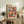 May include: Colorful mushroom art poster in light wood frame displayed on rustic wooden sideboard in modern living room. Vibrant illustration features whimsical spotted mushrooms in pink, orange, teal, and red against dark background. Room styled with fern plant, ceramic vases, books, and neutral furniture creating warm, contemporary home decor setting.
