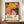 May include: Framed exhibition poster featuring vibrant abstract floral design with yellow chrysanthemum, pink blooms, and black polka dot patterns. Text shows "YAYOI KUSAMA" with Japanese characters and "MUSÉE D'ART MODERNE DE LA VILLE DE PARIS". Poster sits on wooden credenza next to white ceramic vase and stacked books in elegant room with white walls and crown molding.