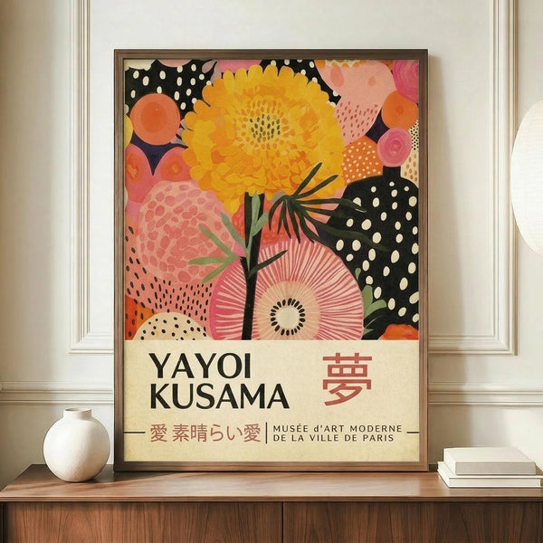 May include: Framed exhibition poster featuring vibrant abstract floral design with yellow chrysanthemum, pink blooms, and black polka dot patterns. Text shows "YAYOI KUSAMA" with Japanese characters and "MUSÉE D'ART MODERNE DE LA VILLE DE PARIS". Poster sits on wooden credenza next to white ceramic vase and stacked books in elegant room with white walls and crown molding.