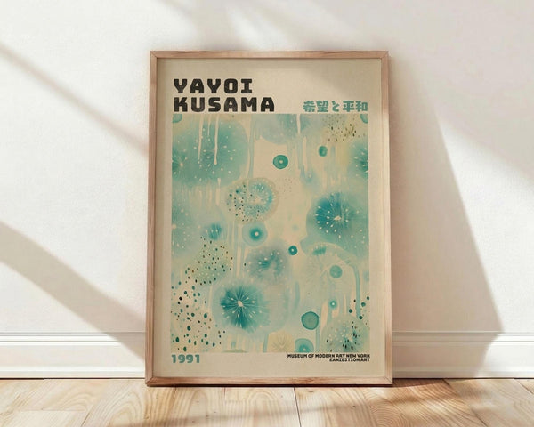 May include: Framed vintage-style exhibition poster featuring abstract organic shapes in turquoise and teal against cream background, displayed on light wood floors against white wall with natural window light casting shadows. Wooden frame surrounds artwork with bold black text at top, Japanese characters, scattered polka dot patterns, and flowing botanical-inspired forms throughout the composition.